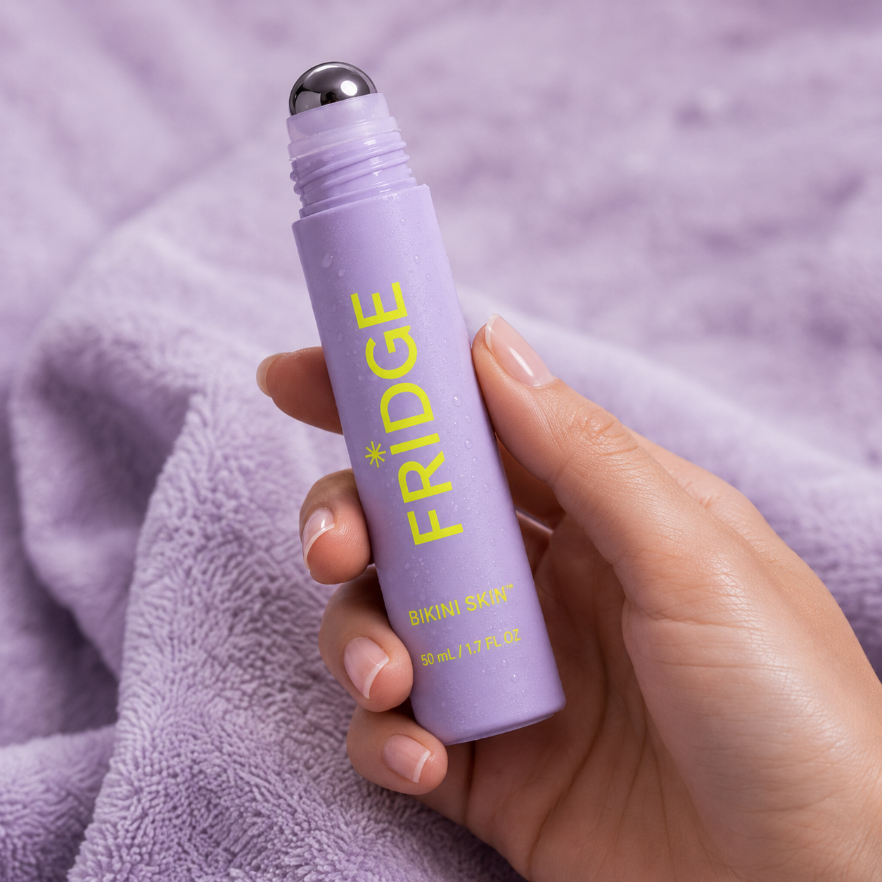 FRIDGE Bikini Skin cooling roller held in hand against lavender towel